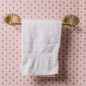 May include: A white towel hangs on a gold towel bar with decorative shell-shaped ends. The towel bar is mounted on a pink and white floral wallpaper.