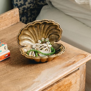 May include: A gold-coloured seashell-shaped trinket box with a beaded necklace and a green beaded bracelet inside.