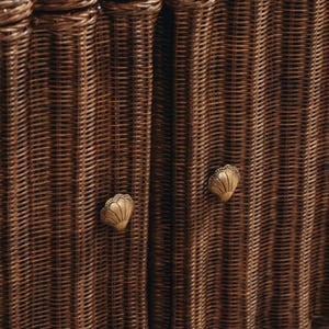 May include: Close-up of a woven wicker cabinet with two doors. The cabinet is a warm brown colour and features two decorative, gold-coloured seashell-shaped knobs. The wicker has a tight weave pattern.