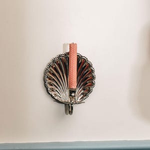 May include: A silver wall-mounted candle holder shaped like a seashell with a pink candle inside.