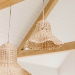 K&ouml;nnte beinhalten: Zwei geflochtene H&auml;ngeleuchten aus Weide h&auml;ngen an einer Holzdecke. Die Leuchten haben die Form von Glocken mit einem breiten, ausgestellten Boden.