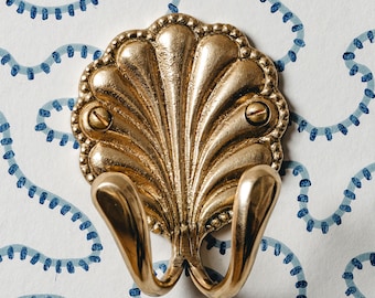 May include: A gold-toned metal double hook in the shape of a seashell. The hook has a decorative, scalloped design.