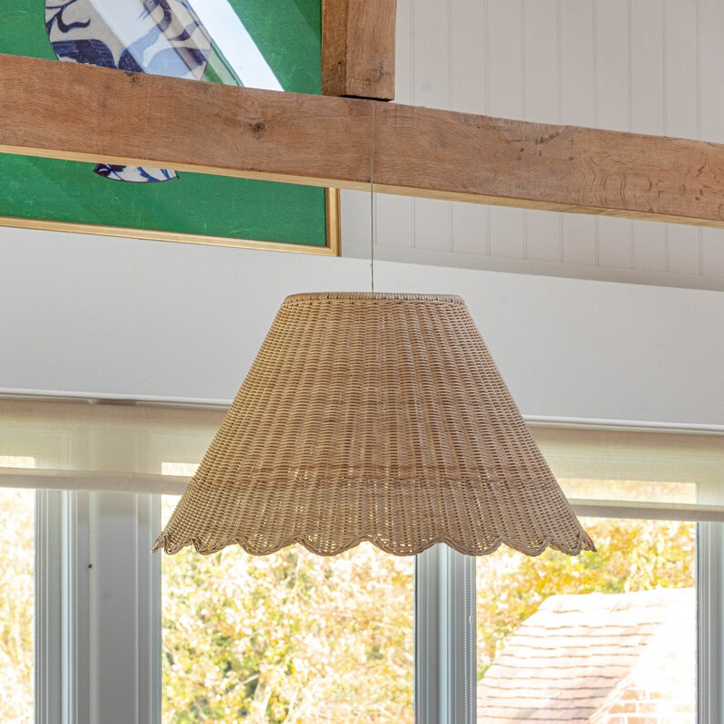 May include: A woven wicker pendant light fixture with a scalloped edge hangs from a wooden beam. The light fixture is a natural beige color.