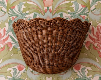 May include: A brown wicker basket with a scalloped edge. The basket is empty and has a natural woven texture.