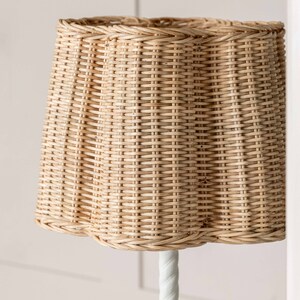 K&ouml;nnte beinhalten: Ein geflochtener Lampenschirm aus Weide in nat&uuml;rlicher beige Farbe. Der Lampenschirm hat einen gewellten Rand und ein geflochtenes Muster.