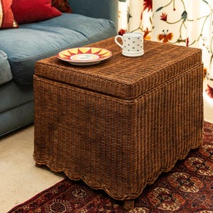 Può includere: Un pouf di vimini marrone con un bordo a festoni. Una tazza in ceramica bianca con cuori blu e un piatto rosso e giallo sono sopra il pouf.