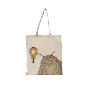 Puede incluir: Una bolsa de tela beige con una bombilla y una polilla con ojos grandes impresos en ella.