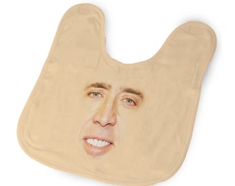 May include: A beige baby bib featuring a printed image of Nicolas Cage's face.