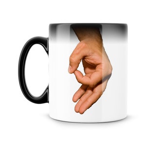 May include: A black and white color-changing mug with a hand making the "okay" gesture on the white side.