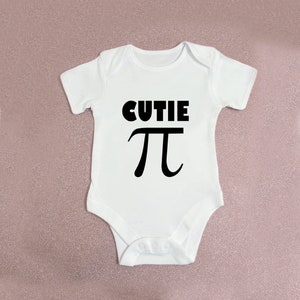 May include: White baby onesie with black text that says "cutie pi".