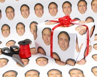 May include: White gift wrap with a red ribbon and a repeating pattern of Nicolas Cage's face. A pair of scissors and a spool of red ribbon are also included in the image.