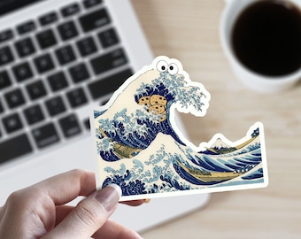 May include: A sticker featuring a blue and white wave with a mountain in the background. The wave has googly eyes and is holding a stack of chocolate chip cookies.