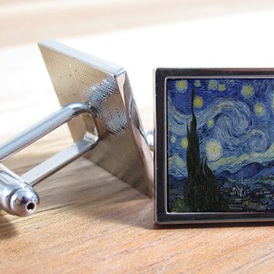 以下が含まれることがあります： 星月夜を描いた正方形の画像がついた、銀製のカフスボタンのペア。カフスボタンは金属製で、磨かれた仕上げになっています。