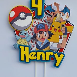 May include: A colourful Pokemon cake topper featuring a red and white Pokeball, a blue and green Squirtle, a yellow Pikachu, a red and orange Charizard, a blue number 4, a character from the Pokemon anime wearing a red hat and a blue shirt, and the name "Henry" in yellow letters with a blue outline.
