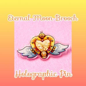 May include: A holographic pin shaped like a heart with wings, featuring gold-toned edges, a faceted center, and small circular accents. The text Eternal Moon Brooch and Holographic Pin is displayed in white font above and below the pin design.