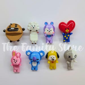 Puede incluir: Una colección de nueve figuras de personajes de dibujos animados de colores. Las figuras incluyen un personaje marrón, una oveja blanca, un conejo morado, un corazón rojo, un conejo rosa, un koala azul, un perro amarillo y un personaje gris. El texto The Family Store es visible.