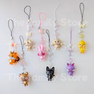 Peut inclure: Une collection de breloques de téléphone colorées avec diverses figurines d'animaux, dont un tigre, un ours, un lapin, un chien, un chat et un poussin. Chaque breloque est ornée de perles et d'éléments décoratifs, tels que des papillons et des cœurs, et possède une boucle noire ou rose.
