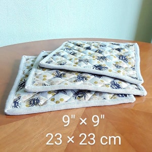 Può includere: Tre presine in lino da 23 cm x 23 cm con un motivo a nido d'ape e api. Le presine sono di colore grigio chiaro con un bordo grigio scuro e un motivo a nido d'ape giallo. Le api sono nere con strisce gialle.