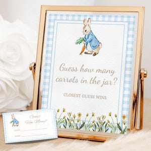 May include: A framed sign with a gold-coloured metal frame featuring a watercolour illustration of a rabbit holding a carrot. The sign reads "Guess how many carrots in the jar?" and "Closest Guess Wins". A matching card is also present.