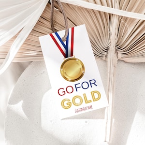Könnte beinhalten: Ein weißes Etikett mit einem rot-weiß-blauen Band und einer goldenen Medaille. Das Etikett lautet "GO FOR GOLD" in roten und goldenen Buchstaben. Der Text "CUSTOMIZE HERE" steht in kleineren goldenen Buchstaben unter dem Haupttext.