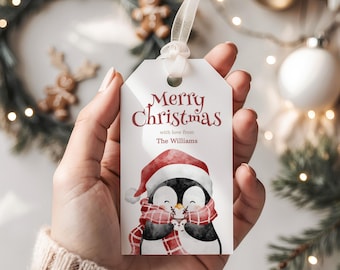 May include: A white Christmas gift tag with the text "Merry Christmas" in burgundy script. Below, a watercolor illustration of a penguin wearing a Santa hat and a red and white scarf. The tag includes the text "with love from The Williams".