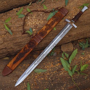 May include: A silver sword with a wooden scabbard decorated with intricate carvings. The sword has a leather grip and a silver blade with a runic inscription that reads "VERFIST: HIMR".