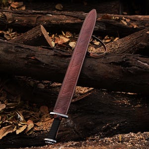 May include: A brown leather-wrapped sword with a black handle lies on a pile of brown tree logs. The sword has a decorative pattern on the leather wrapping.