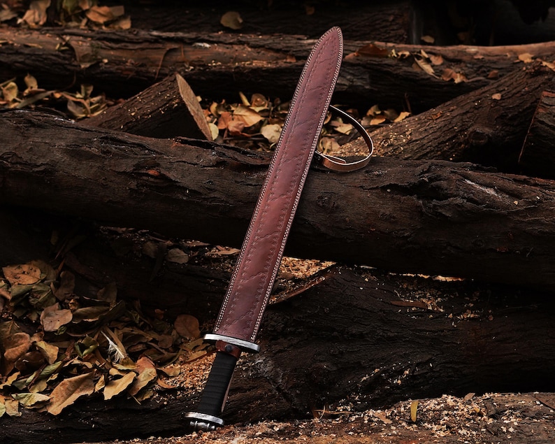 May include: A brown leather-wrapped sword with a black handle lies on a pile of brown tree logs. The sword has a decorative pattern on the leather wrapping.