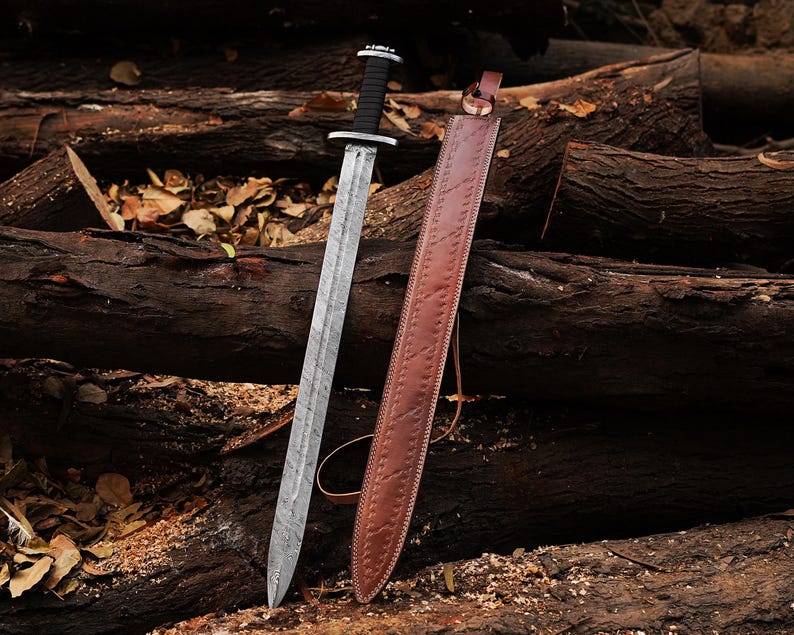 May include: A silver sword with a black handle and a brown leather scabbard. The sword and scabbard are lying on a pile of brown logs.