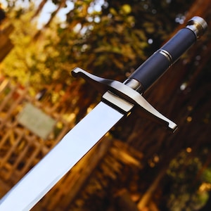 May include: A silver and black sword with a long, sharp blade and a black handle. The sword is in focus, while the background is blurred.
