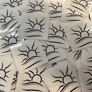 May include: A stack of white square stickers with a black silhouette of a sun rising over a wavy line.