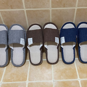 May include: Six pairs of indoor slippers in various colors, including gray, brown, and blue. The slippers are made of a soft, textured fabric and have a simple, comfortable design.