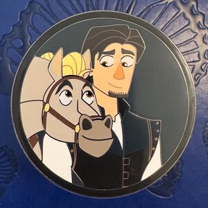 Könnte beinhalten: Runder Ansteckpin mit einer Cartoon-Illustration eines Mannes und eines Pferdes. Der Mann hat dunkles Haar und trägt eine schwarze Weste. Das Pferd hat einen Zaum. Der Pin hat einen silbernen Rand und einen dunkelblauen Hintergrund.
