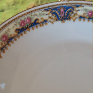 以下が含まれることがあります： 金と青の縁取りが施された白い磁器のボウル。縁取りは花柄と金のアクセントで飾られています。