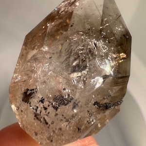 Peut inclure: Un cristal de quartz clair avec des inclusions noires. Le cristal est doublement terminé et a une surface naturelle et rugueuse.