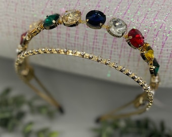 May include: A gold headband with a row of colorful rhinestones. The rhinestones are green, gold, blue, clear, red, and yellow.