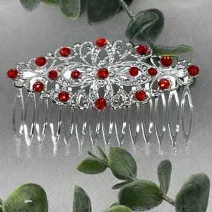 May include: Silver hair comb with a decorative design featuring a floral pattern and red rhinestones.