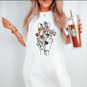 May include: White oversized t-shirt with a peace sign graphic featuring colorful flowers.