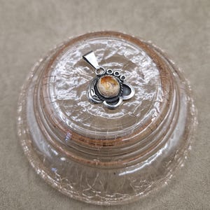 May include: A silver pendant with a brown and white stone set in a silver flower design.