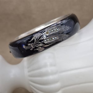 May include: A dark blue enamel bangle bracelet with a silver wheat design and small pearl accents. The bracelet has a silver interior and a hinged clasp. The wheat design is detailed and elegant, adding a touch of vintage charm.