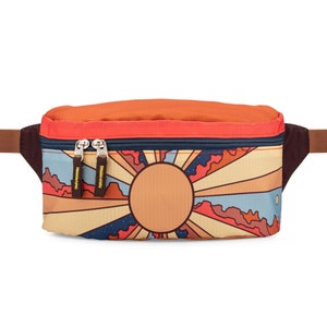 Front of fanny pack. Design features Grand Canyon National Park mountains, desert landscape, and sun with sunbeams. Primary colors are red, yellow, brown and blue.