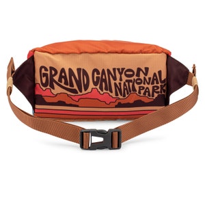 Back of fanny pack and strap with clasped buckle. Design includes "Grand Canyon National Park" text in brown on gold background with mountain artwork.