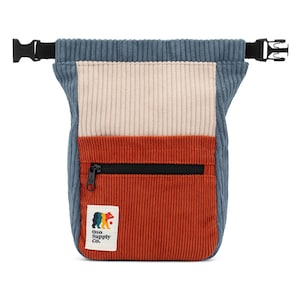 May include: A corduroy fanny pack in blue, cream, and rust colors. The bag has a black zipper pocket and adjustable black straps with buckles. The Oso Supply Co. logo is on a white patch on the front.