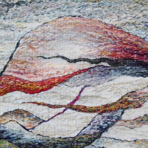 May include: Abstract art piece made with wool fibers in shades of white, red, orange, yellow, blue, and purple. The piece features a large, rounded shape in the center, with smaller, curved shapes surrounding it.