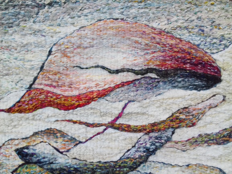 May include: Abstract art piece made with wool fibers in shades of white, red, orange, yellow, blue, and purple. The piece features a large, rounded shape in the center, with smaller, curved shapes surrounding it.