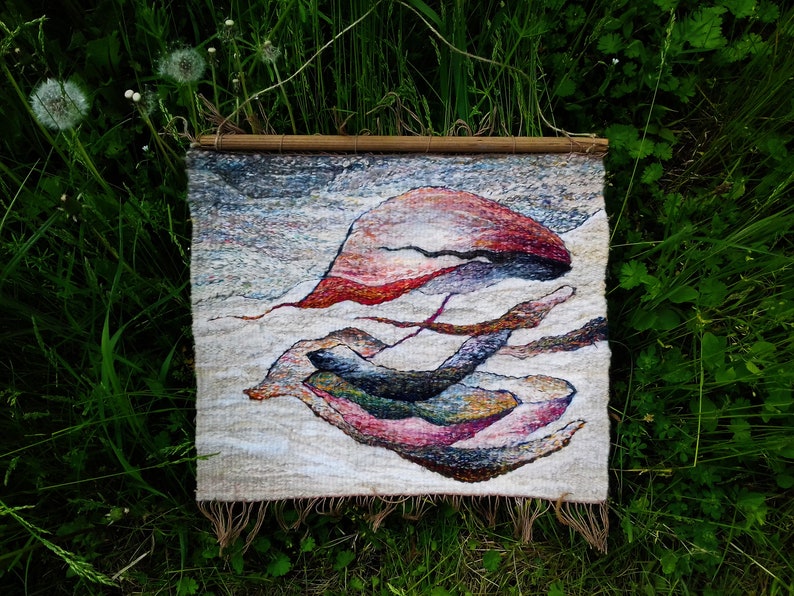 May include: A woven wall hanging with a beige background and abstract shapes in shades of red, pink, purple, blue, and green.