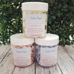 May include: Three clear jars of flavored popcorn with white lids. Each jar has a label that reads "Color Pops" with the flavor and ingredients listed. Flavors include Beach Date, Pitaya Punch, and Berry Blue.