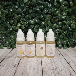May include: Four small clear plastic bottles with white dropper caps, each containing a light yellow liquid. The labels are printed with the text Almond Oil, Peanut Oil, Hazelnut Oil, and Walnut Oil, along with small illustrations and the brand name CrabCuisineCo.