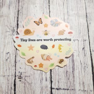 May include: A die-cut sticker with a scalloped edge, featuring various small animals and the text "Tiny lives are worth protecting." The sticker includes illustrations of a snail, butterfly, bee, mouse, frog, and other creatures.