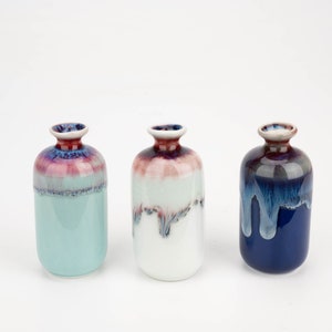 May include: Three ceramic vases with a drip glaze effect. The vases are in shades of blue, white, and light blue. The top of each vase has a red rim.